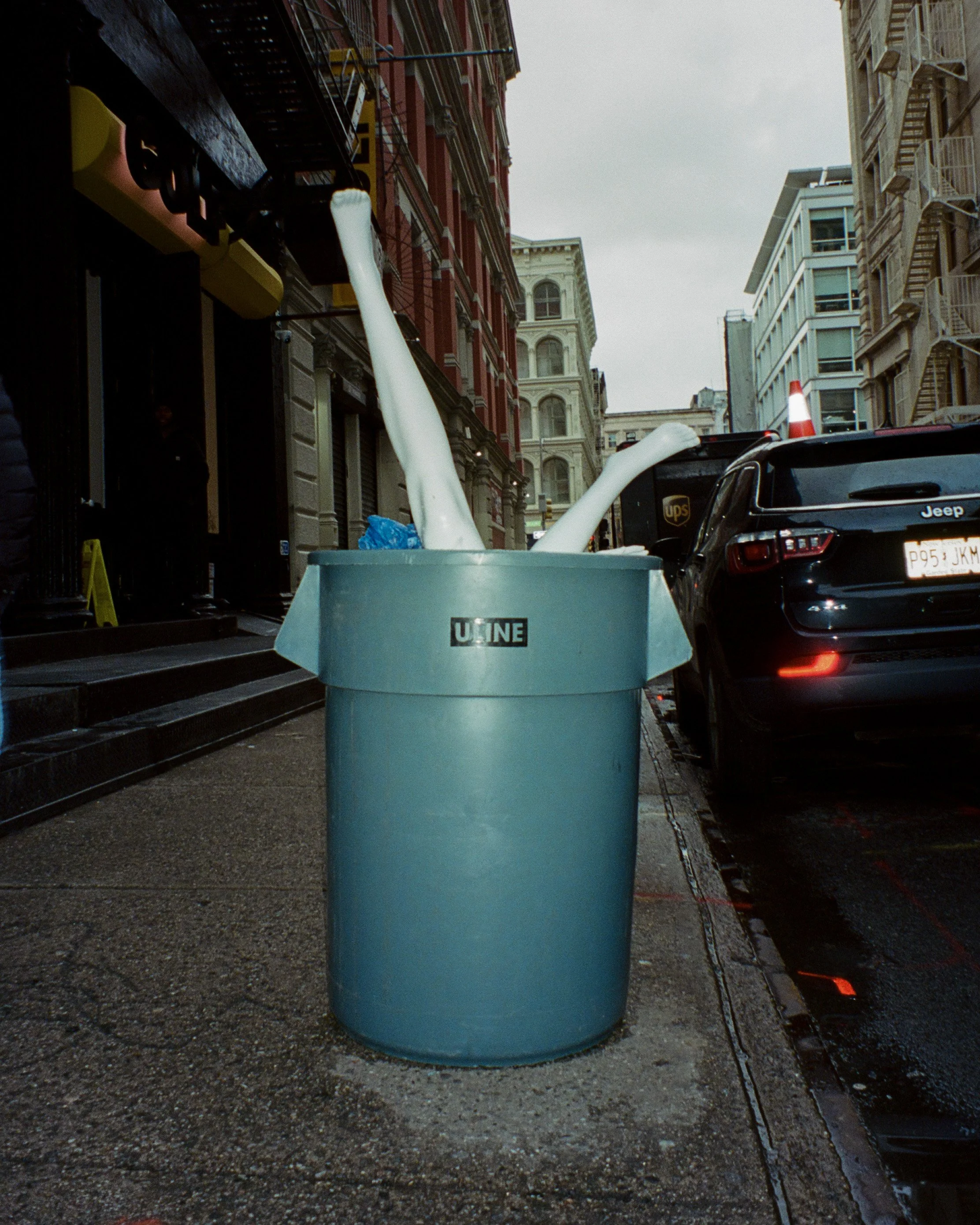 Mannequin legs sticking up out of a trashcan on the street