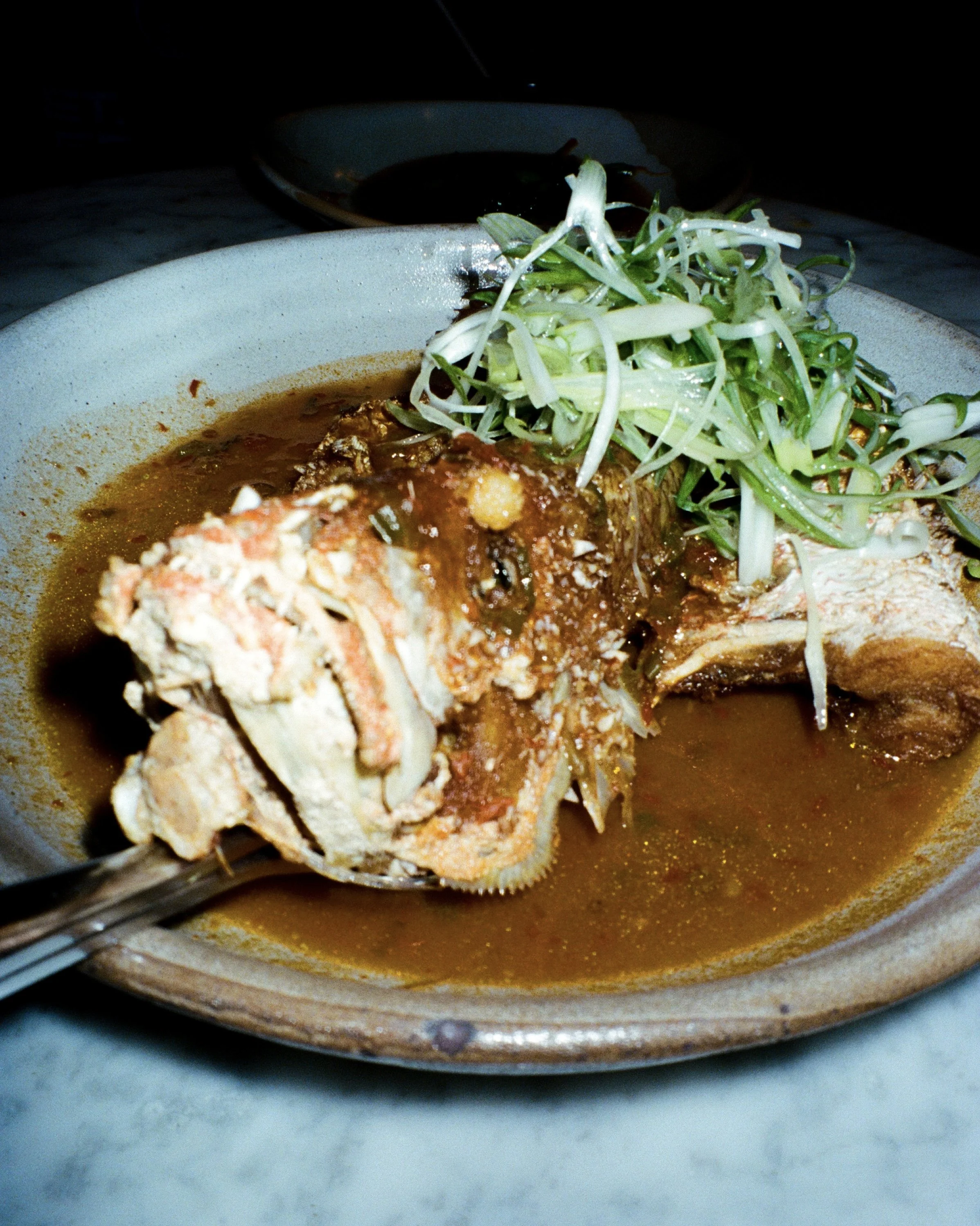A grilled fish on a plate with greens on top