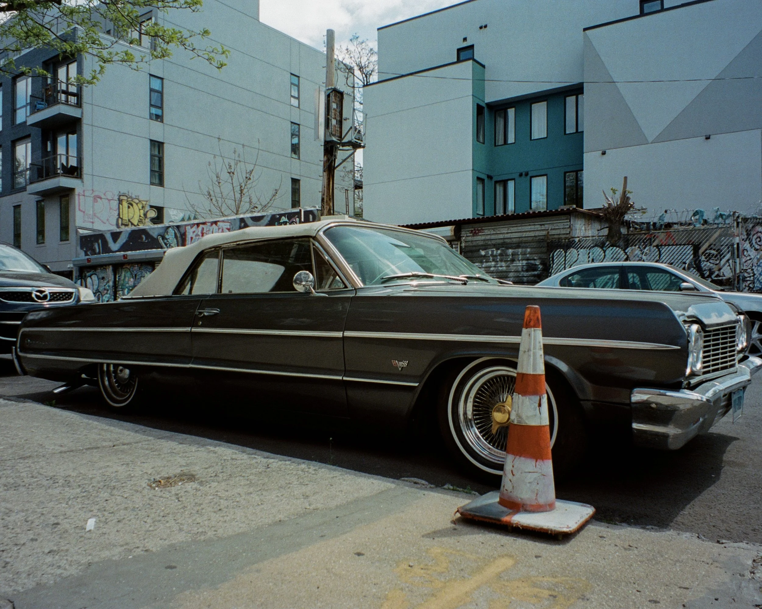 A classic car on the street with a traffic cone in front of it