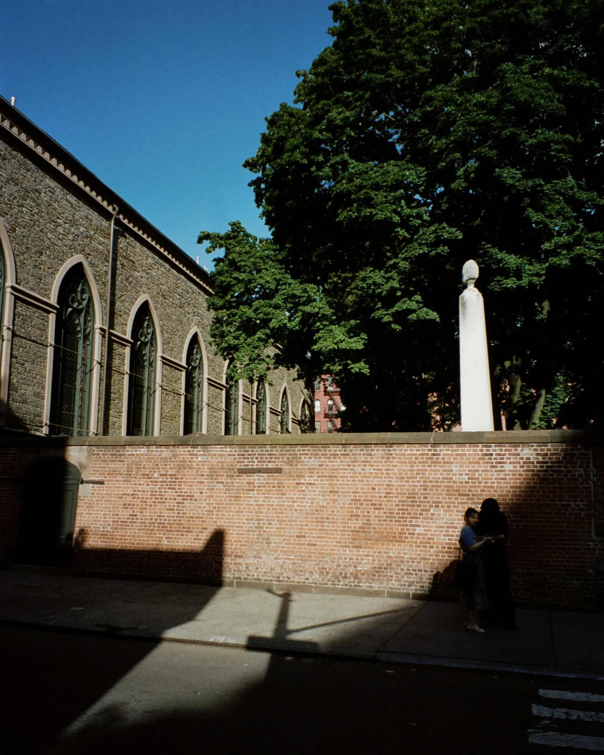 Photo of people walking by a sunlit street with a church in the background