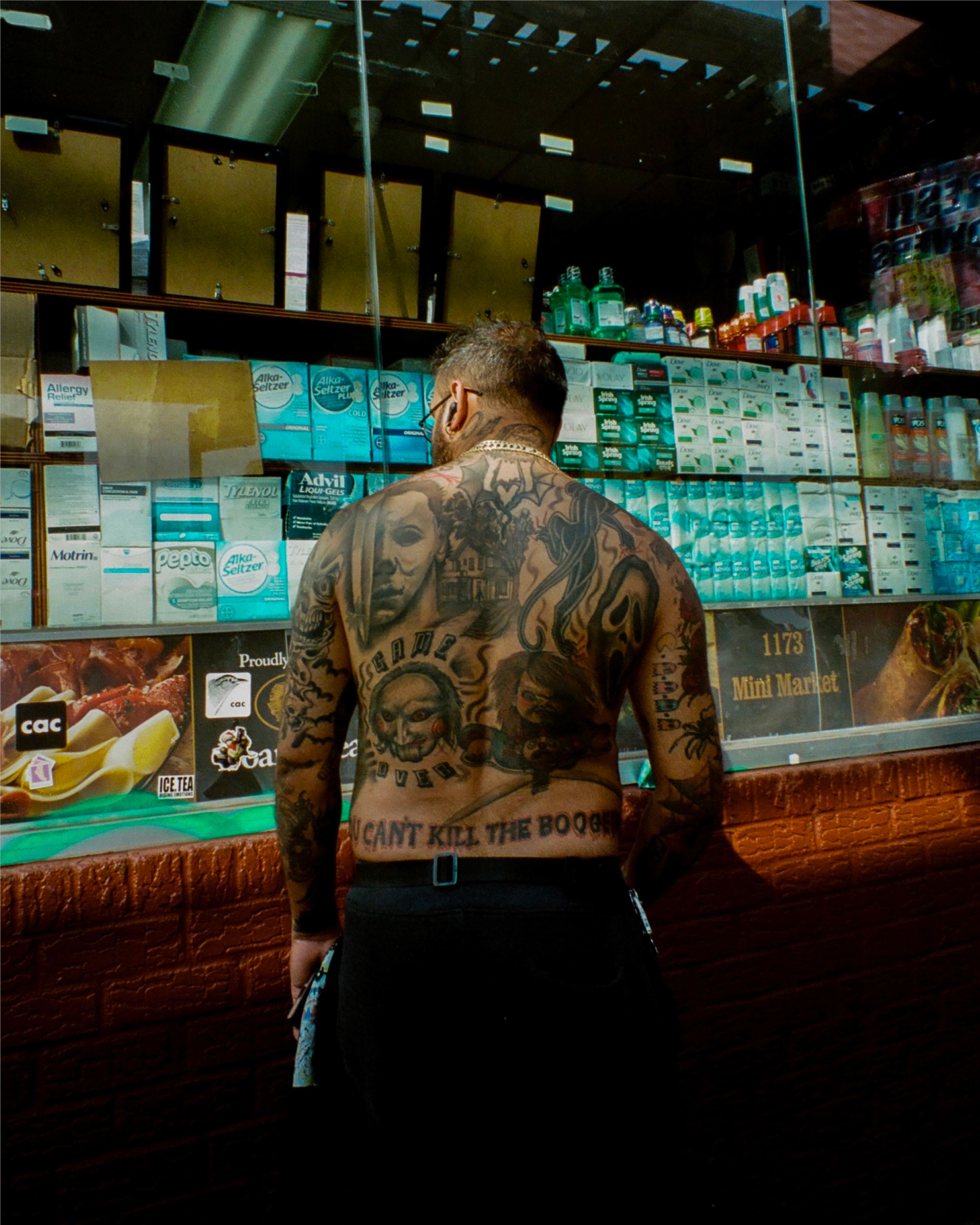 Photo of a man's back covered in horror movie characters in front of a bodega in Brooklyn