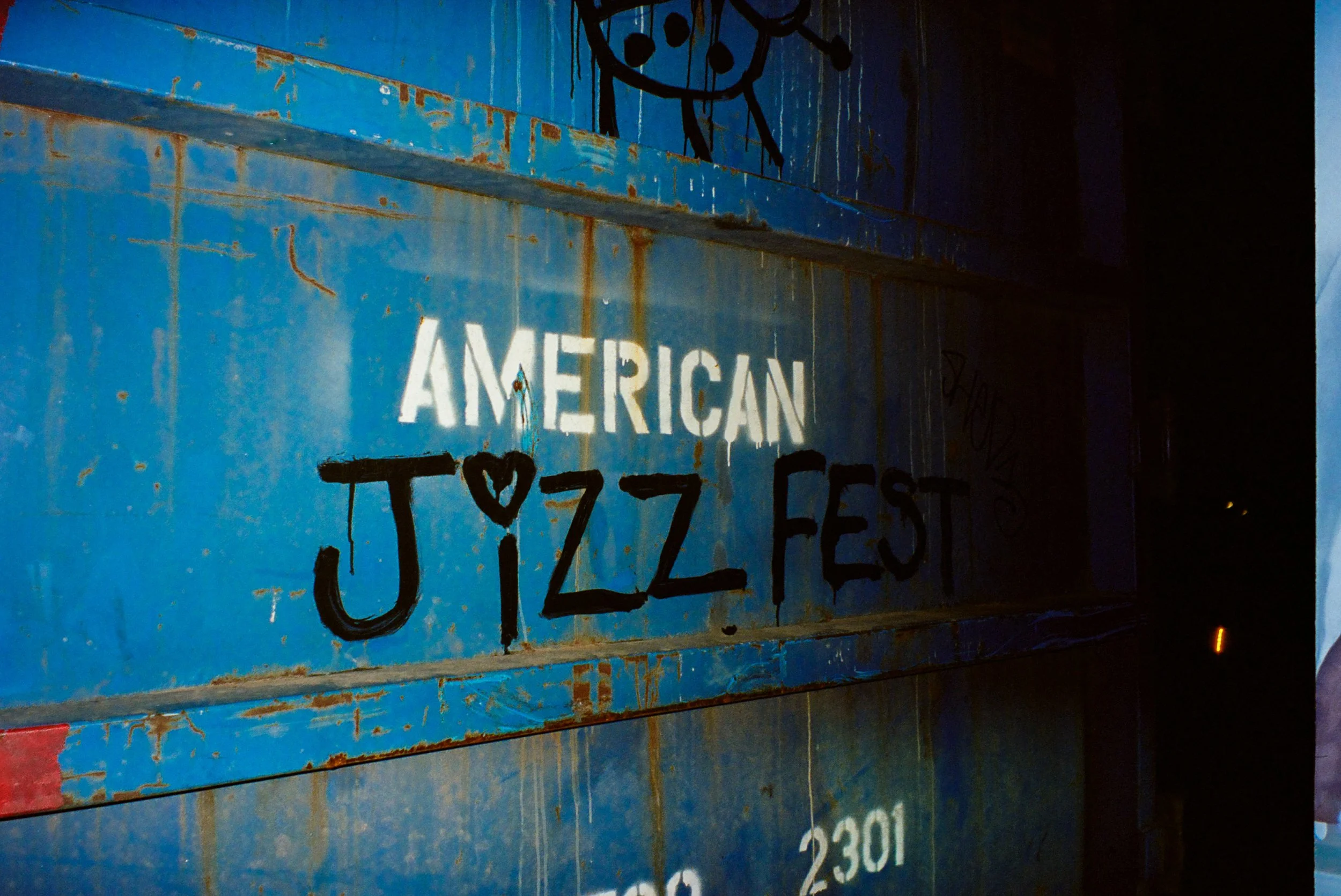 Photo of a dumpster that says "American Jizz Fest"