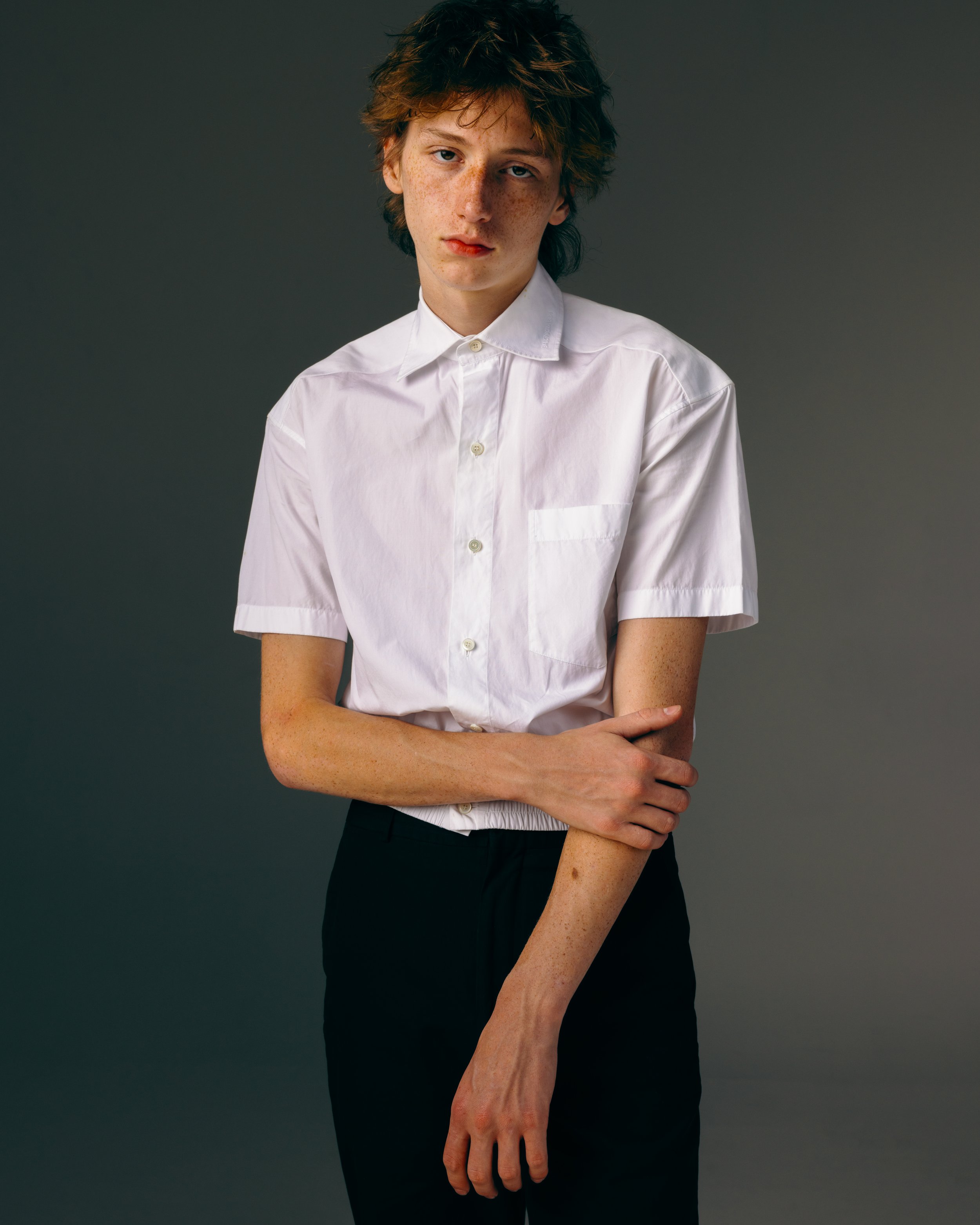 Portrait of a redhead white male model in a short sleeve button down shirt and black pants in a white studio