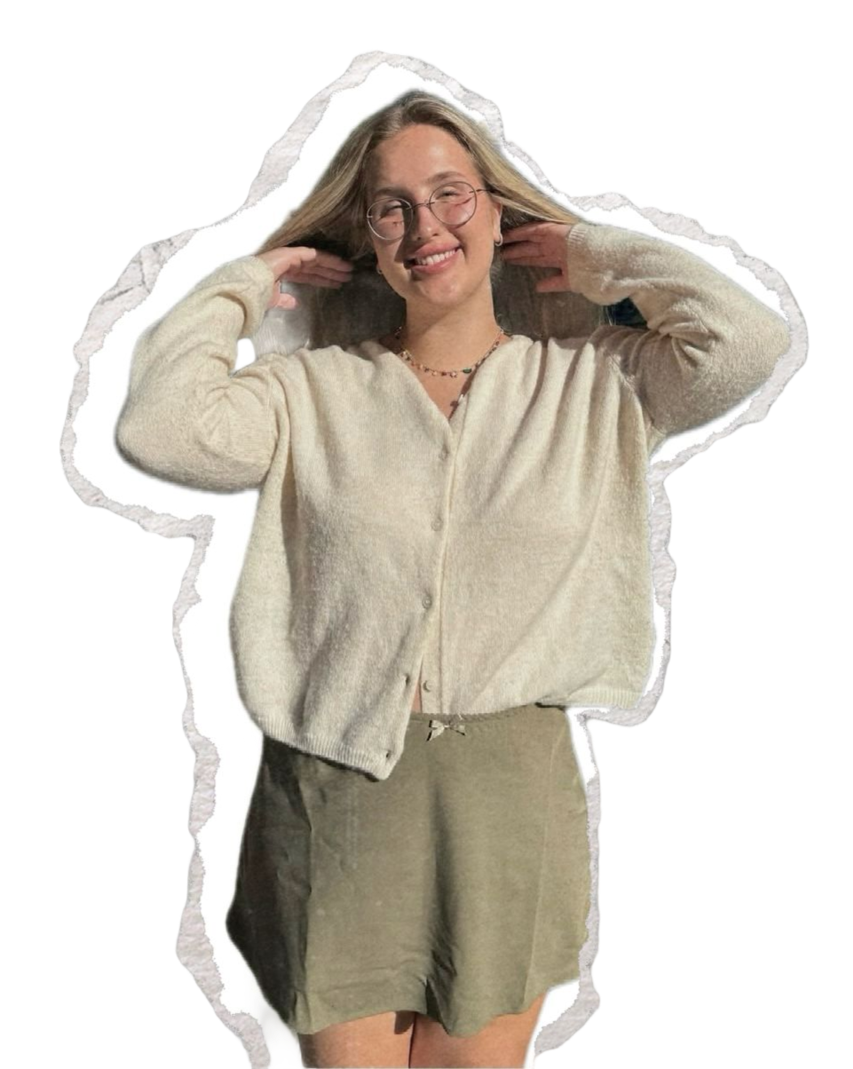 A young woman smiling and winking while adjusting her glasses, wearing a beige cardigan and shorts, with glasses and a necklace.