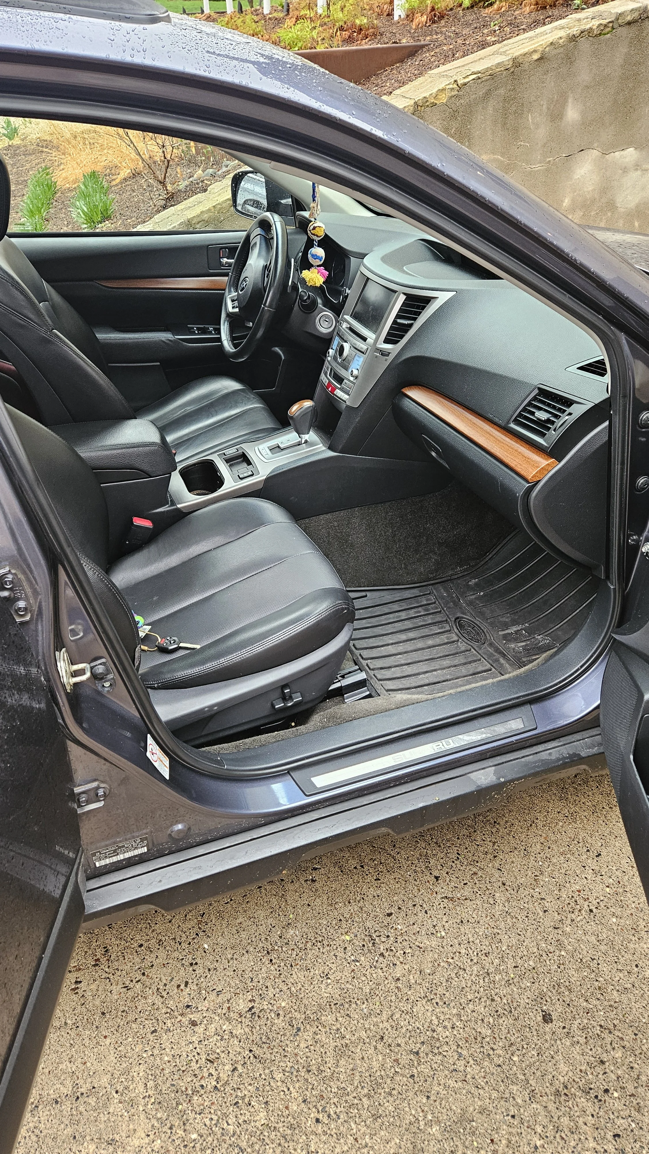 Interior of a black car showing the driver's seat, dashboard, steering wheel, and front passenger seat, with some rain droplets on the top of the window.