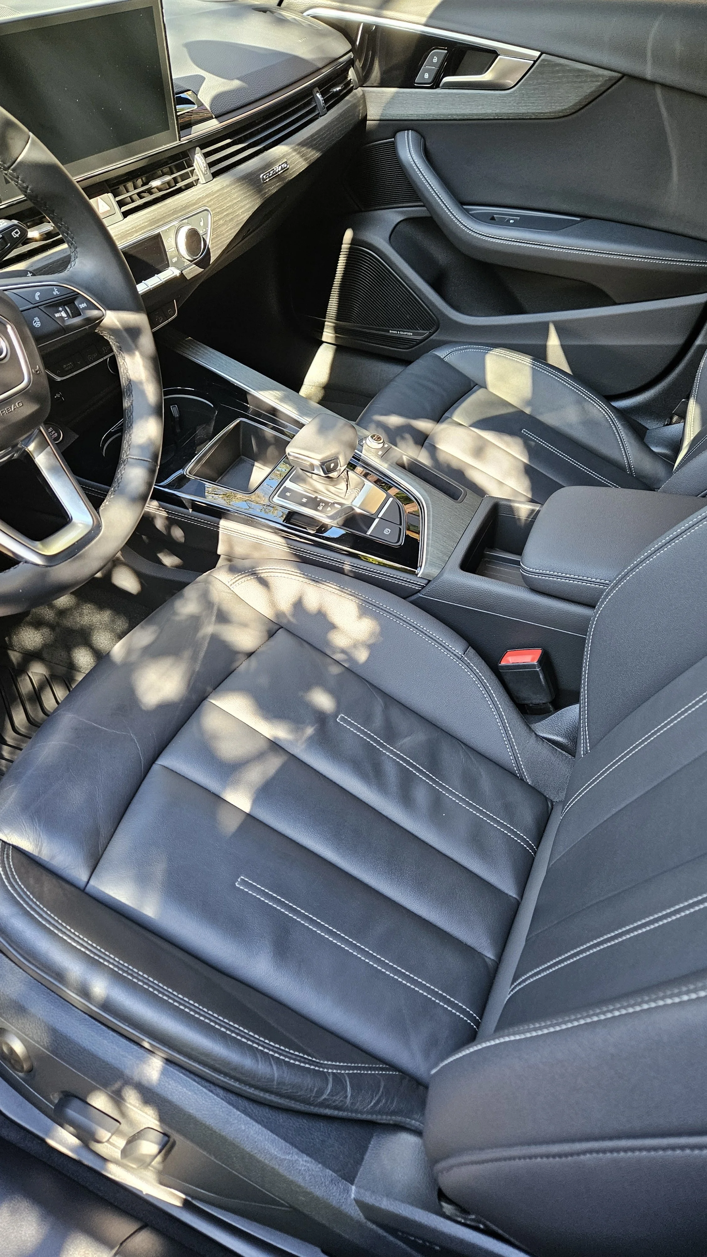 Interior of a modern car showing the driver's seat, center console with gear shifter, and dashboard with a touchscreen display.