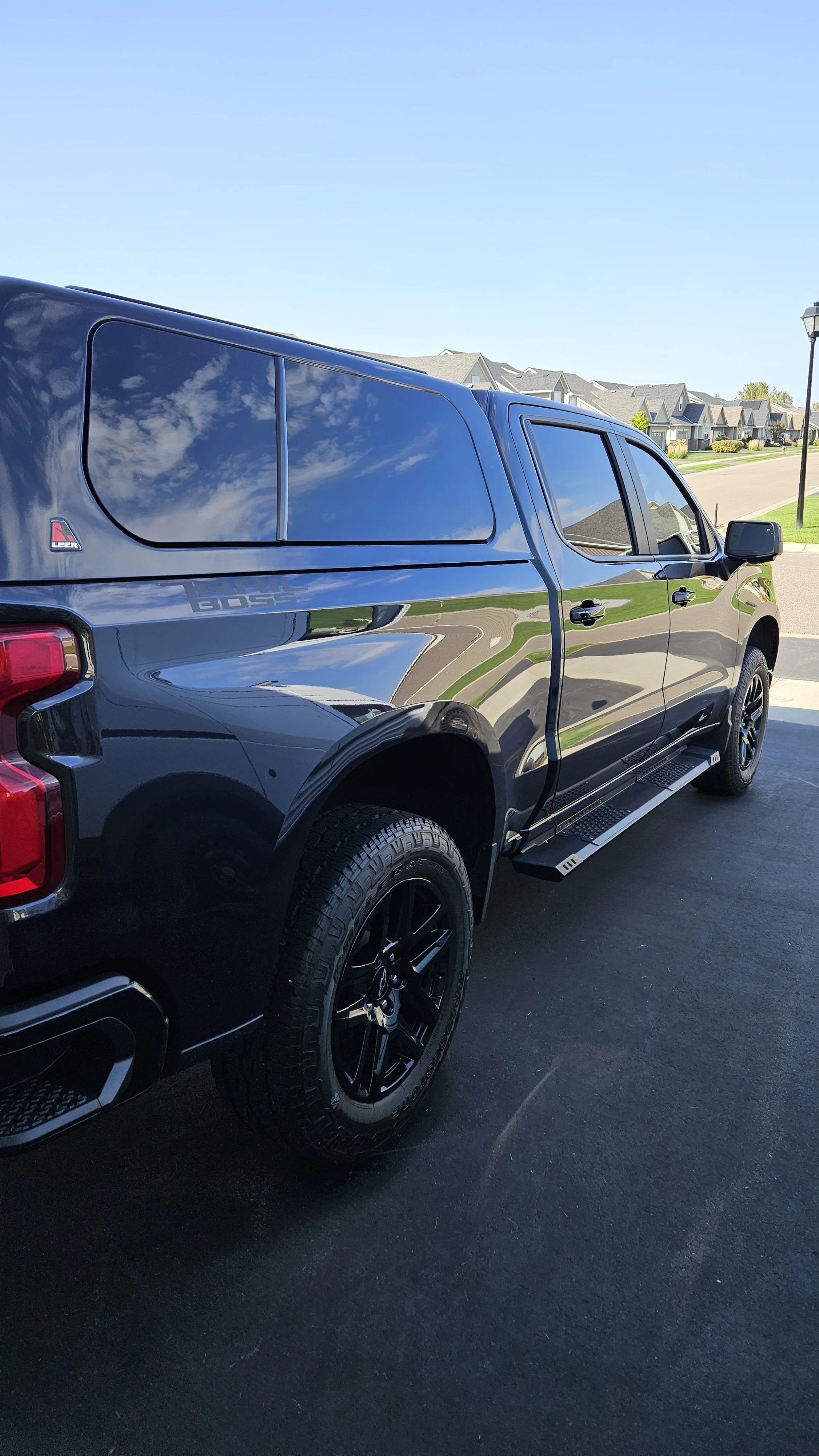 A black pickup truck parked on a driveway in a suburban neighborhood with houses and trees in the background.
