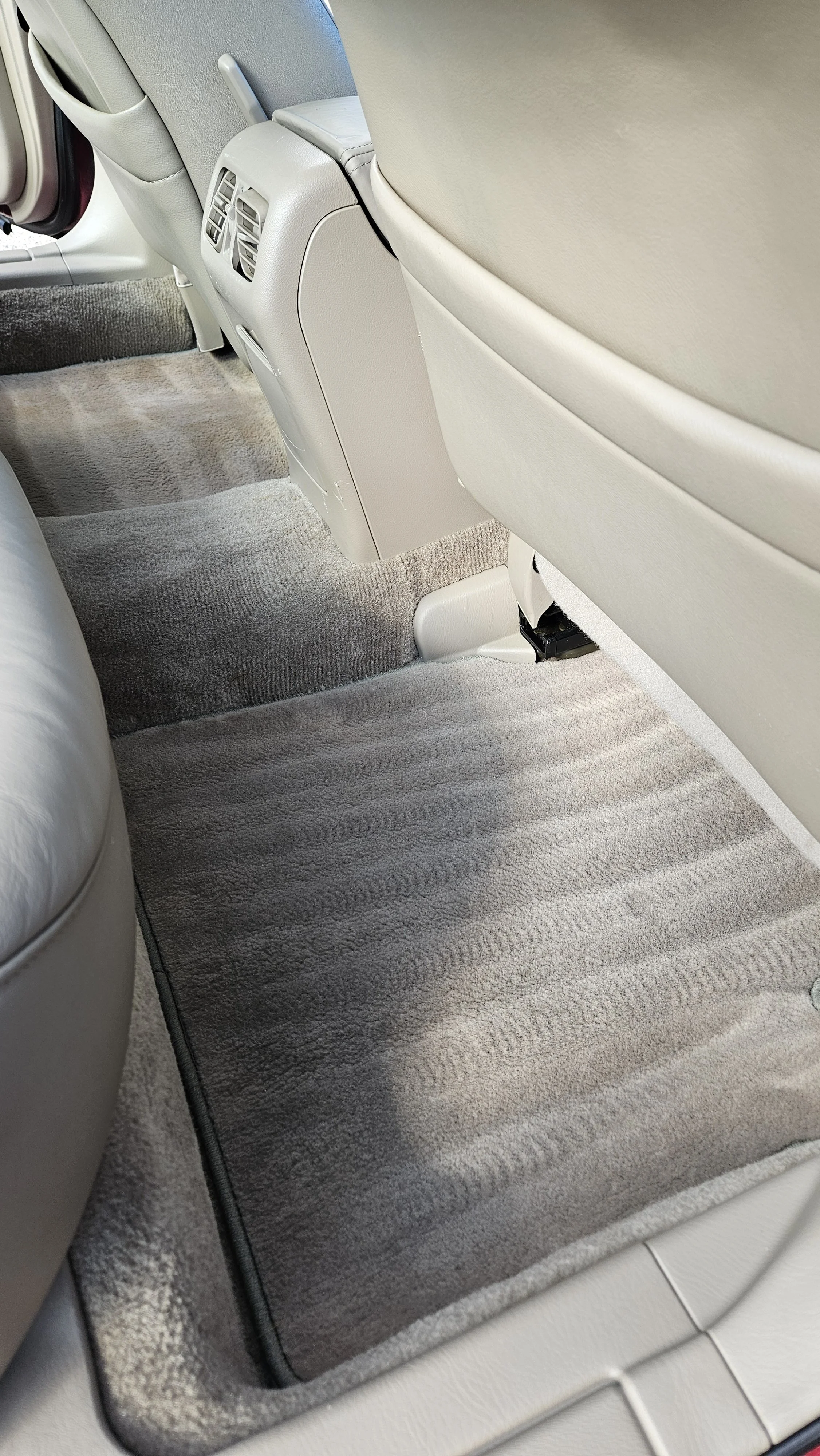 Interior of a vehicle showing gray plush carpeted floor space and back of front seats with beige upholstery.