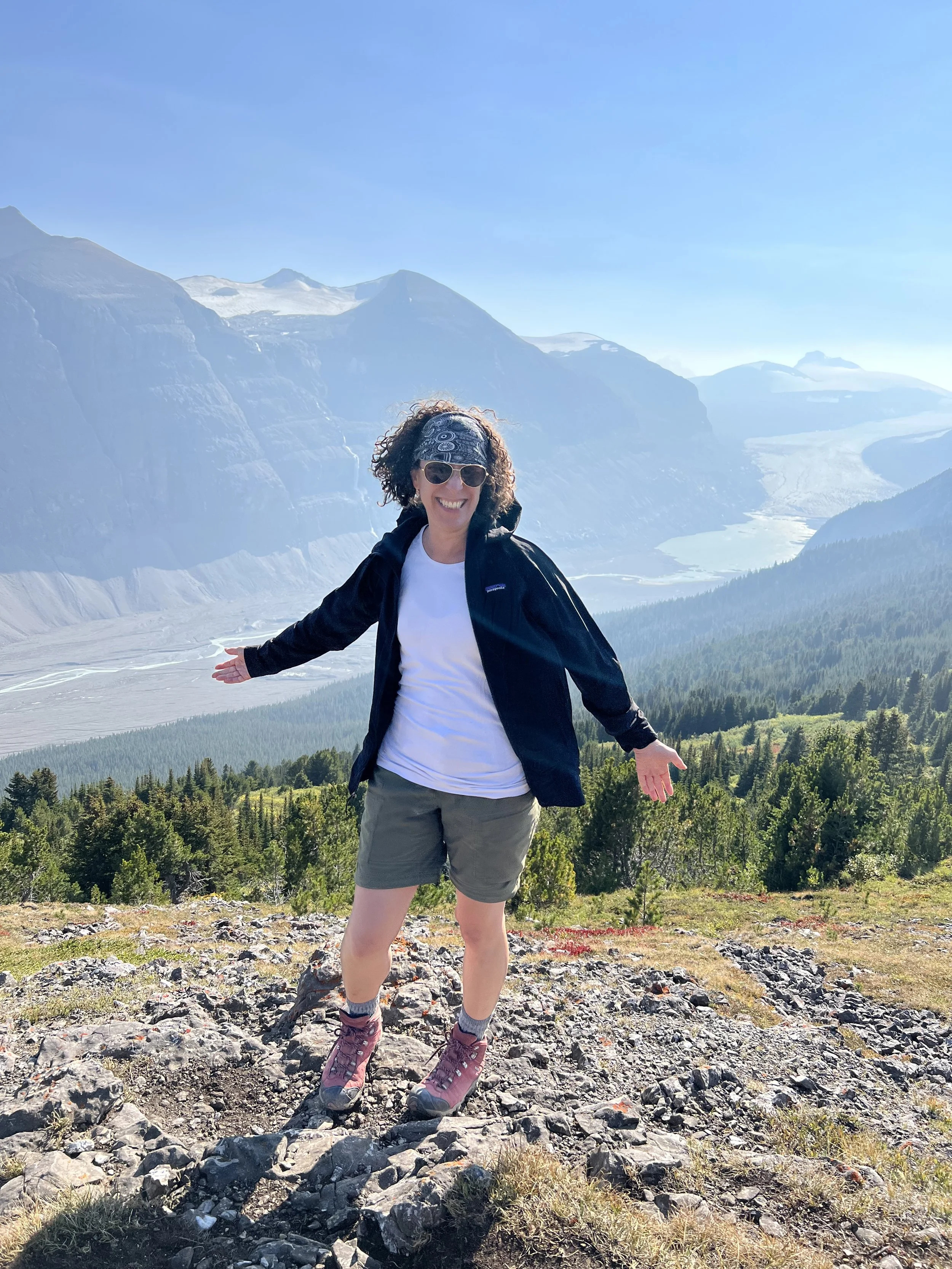 Woman hiking on rocky terrain with mountains and forest in the background