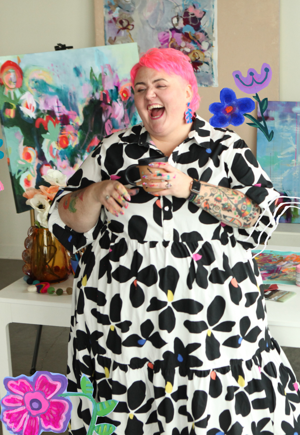 A woman with short pink hair and tattoos on her arms, wearing a black and white dress with a floral pattern, is laughing while holding a mug. She is standing in an art studio with colorful paintings and floral arrangements behind her, with decorative cartoon flowers added to the image.
