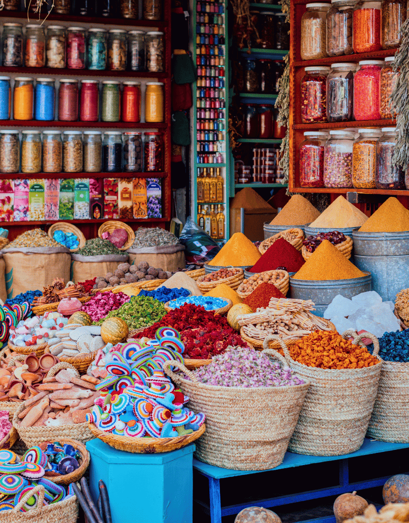 A colorful spice and herbal market stall displaying various dried herbs, spices, and teas in glass jars and baskets.