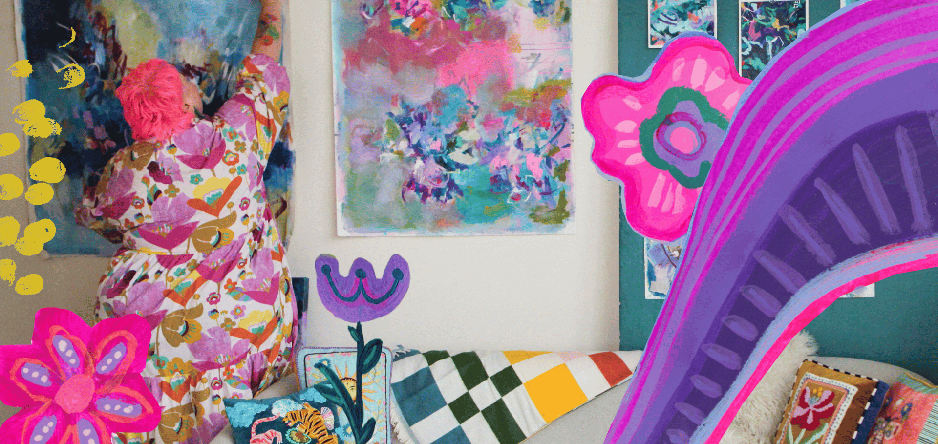 An art gallery with colorful paintings and sculptures. A person with bright pink hair wearing a floral pink, purple, and yellow dress is examining artwork. The room has a variety of vibrant, abstract, and floral art pieces displayed on the walls and sculptures, including large, colorful flowers and a rainbow arch.