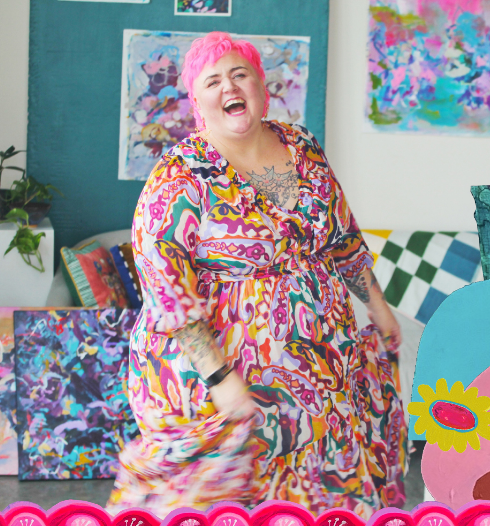 A woman with pink hair laughing and dancing indoors, with colorful artwork on the walls behind her.
