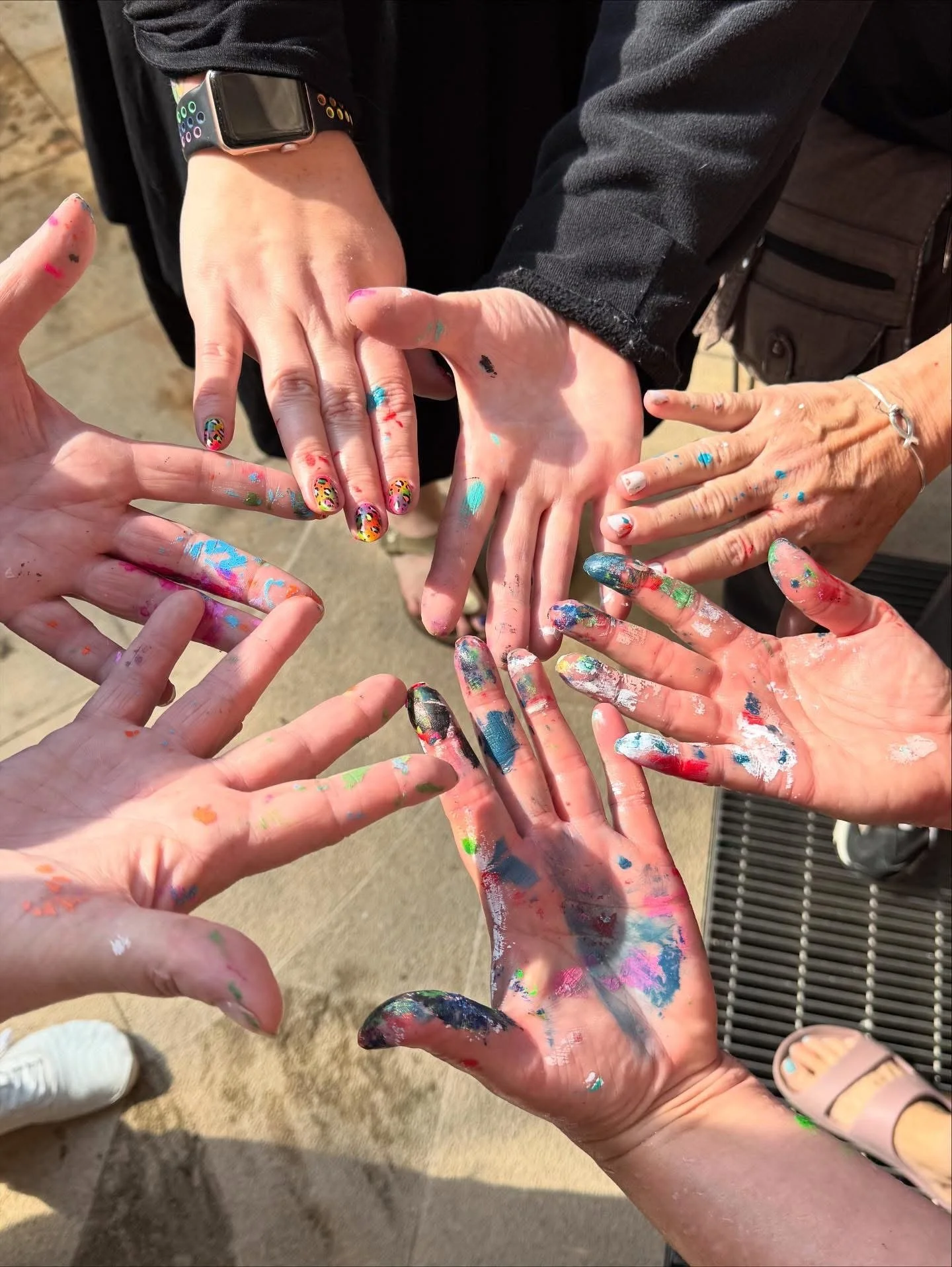 Multiple hands covered in colorful paint, reaching toward each other in a group gesture.