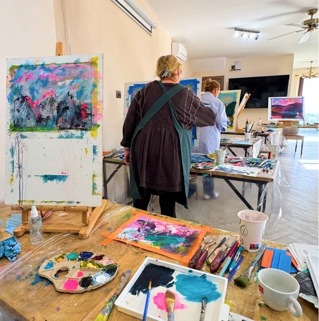 Women painting abstract landscapes in an art studio with easels and supplies.