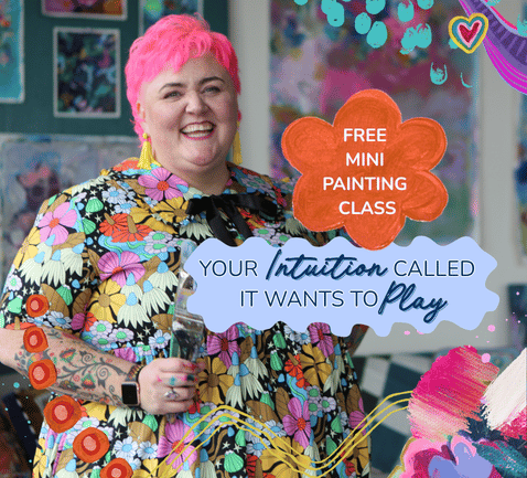A smiling woman with pink hair and colorful floral dress holding a glass at an event advertising a free mini painting class, with vibrant decorations and signs.