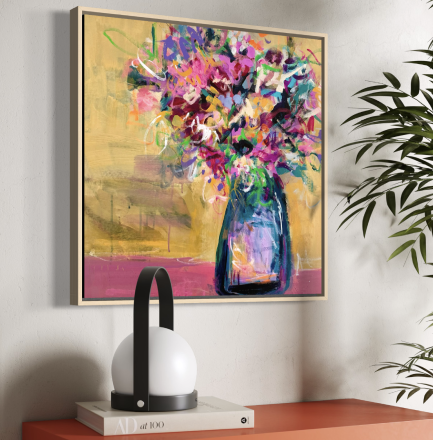 A colorful abstract painting of a flower bouquet in a vase hanging on a white wall, with a black and white modern lamp and a potted plant nearby.