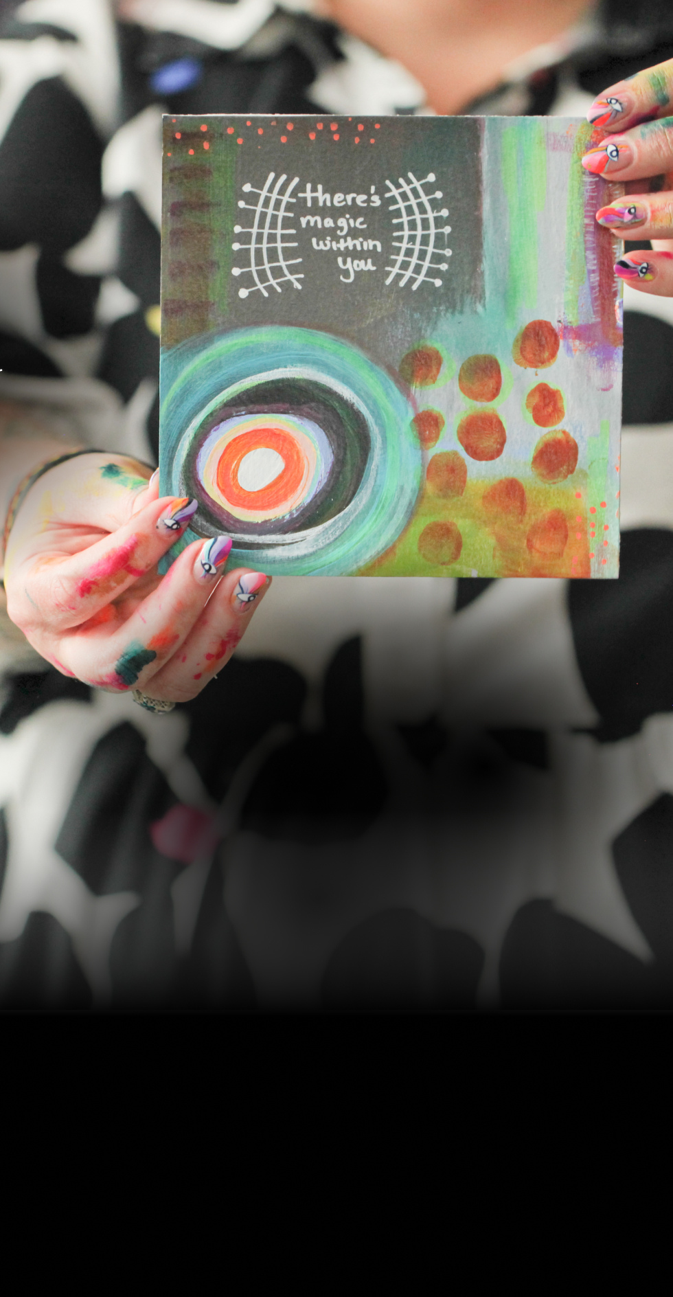 A person with painted fingers holding a colorful abstract painting with a rainbow of colors and the words 'There's magic within you' written at the top.