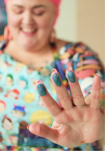 Close-up of a woman's hand with painted nails, her face smiling in the background, wearing a colorful shirt with cartoon characters.