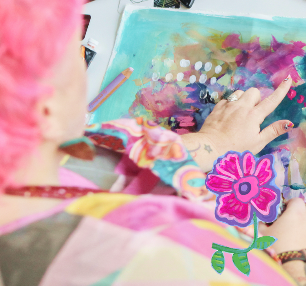 A person with pink hair creating abstract art on a canvas with colorful strokes, dots, and smudges, using various art supplies, including an orange colored pencil, with a cartoon flower sticker on the bottom right of the image.