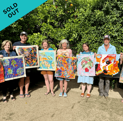 Six people standing outdoors in front of greenery, holding colorful quilt artworks, with a blue banner in the top left corner that says 'SOLD OUT'.
