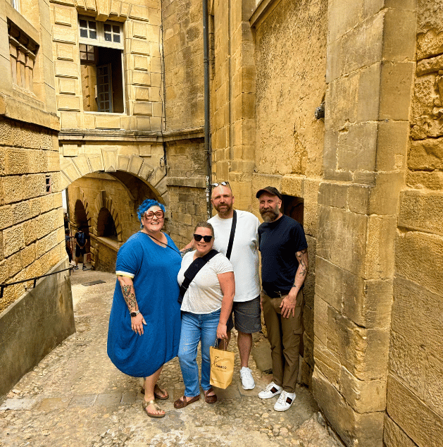 Four people standing together in a historic stone alleyway, smiling at the camera, with arched walkways and old stone buildings in the background.