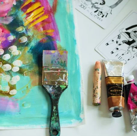 Painting supplies including a paintbrush, tubes of paint, a painting of a Christmas tree with ornaments, and tarot cards.
