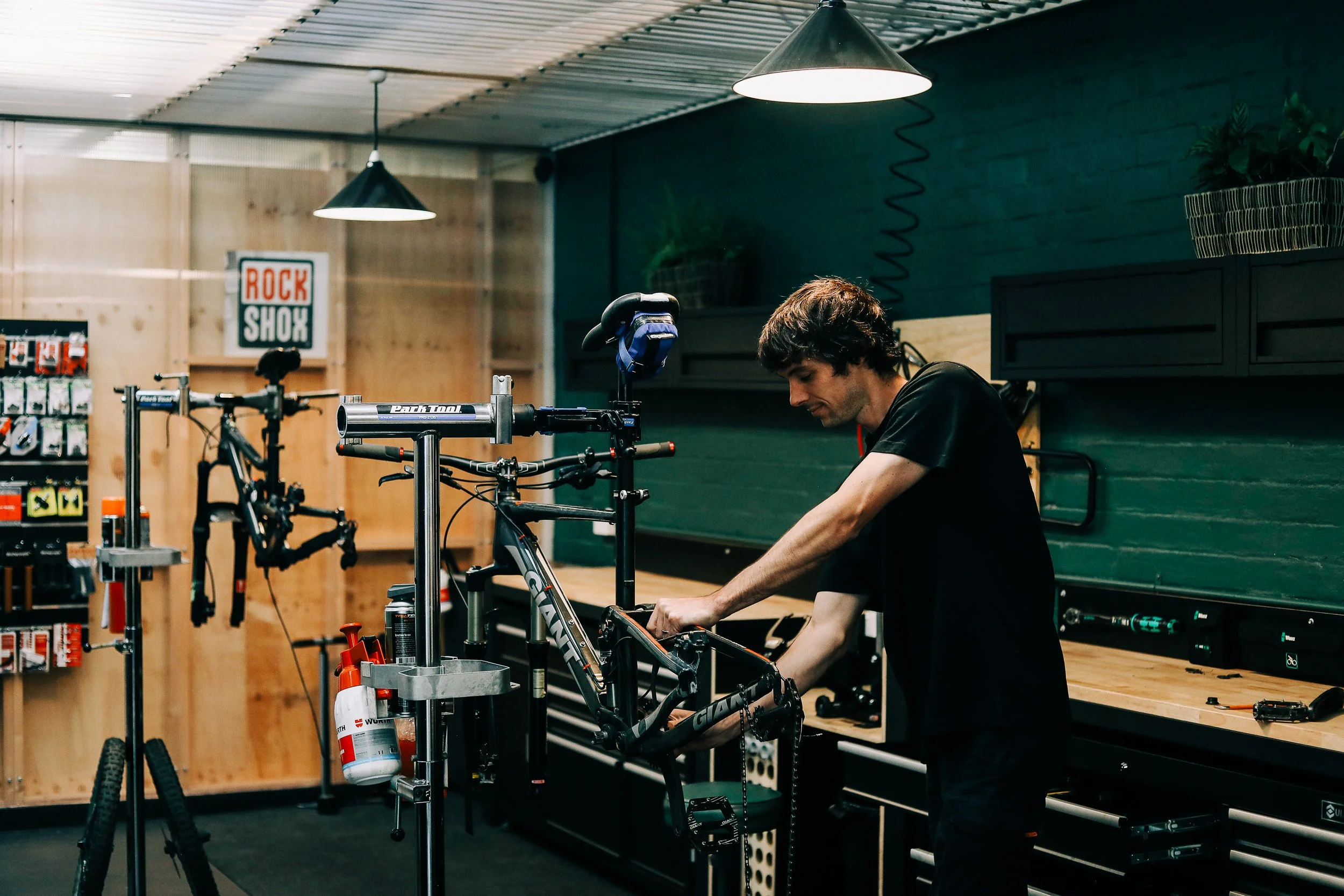 A man working on a bicycle in a workshop, with tools and bike parts around.