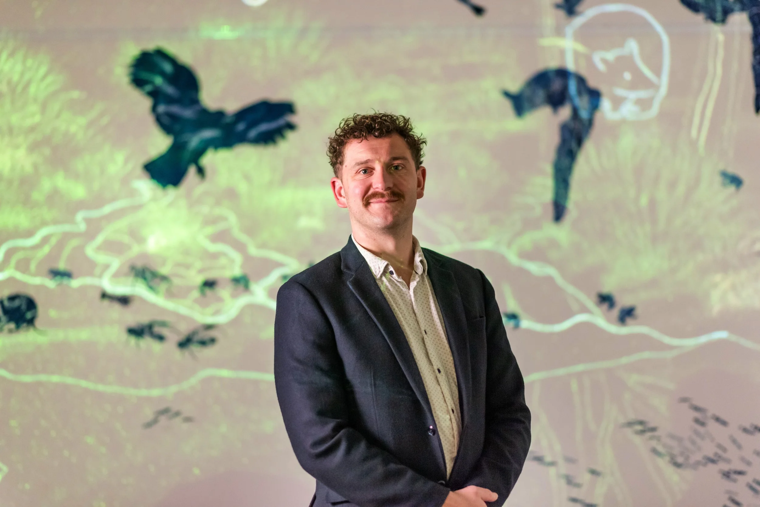 Casey Thomsen wearing a suit jacket standing in front of a colorful abstract background.