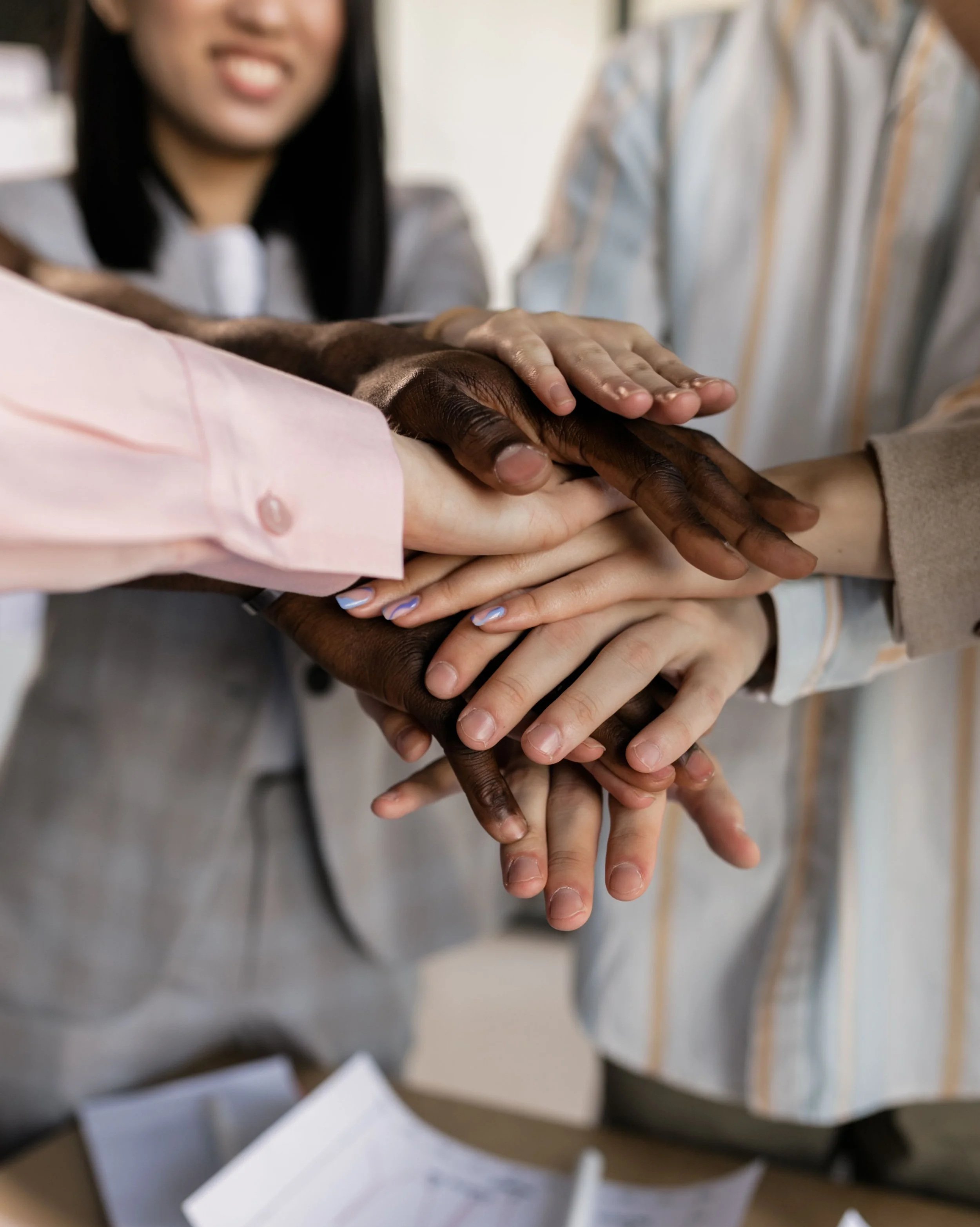 Multiple hands of diverse skin tones stacked on top of each other in a show of teamwork or unity.
