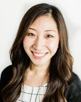 Close-up of an Asian woman with long brown hair smiling against a white background.