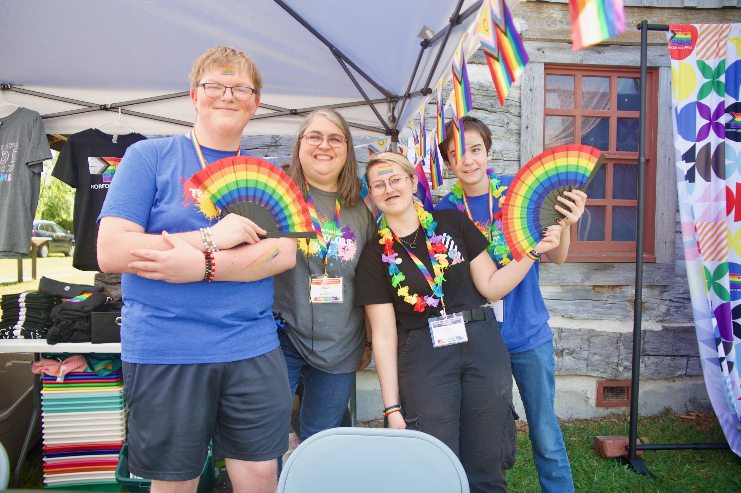 Four smiling people with rainbow fans and rainbow necklaces.