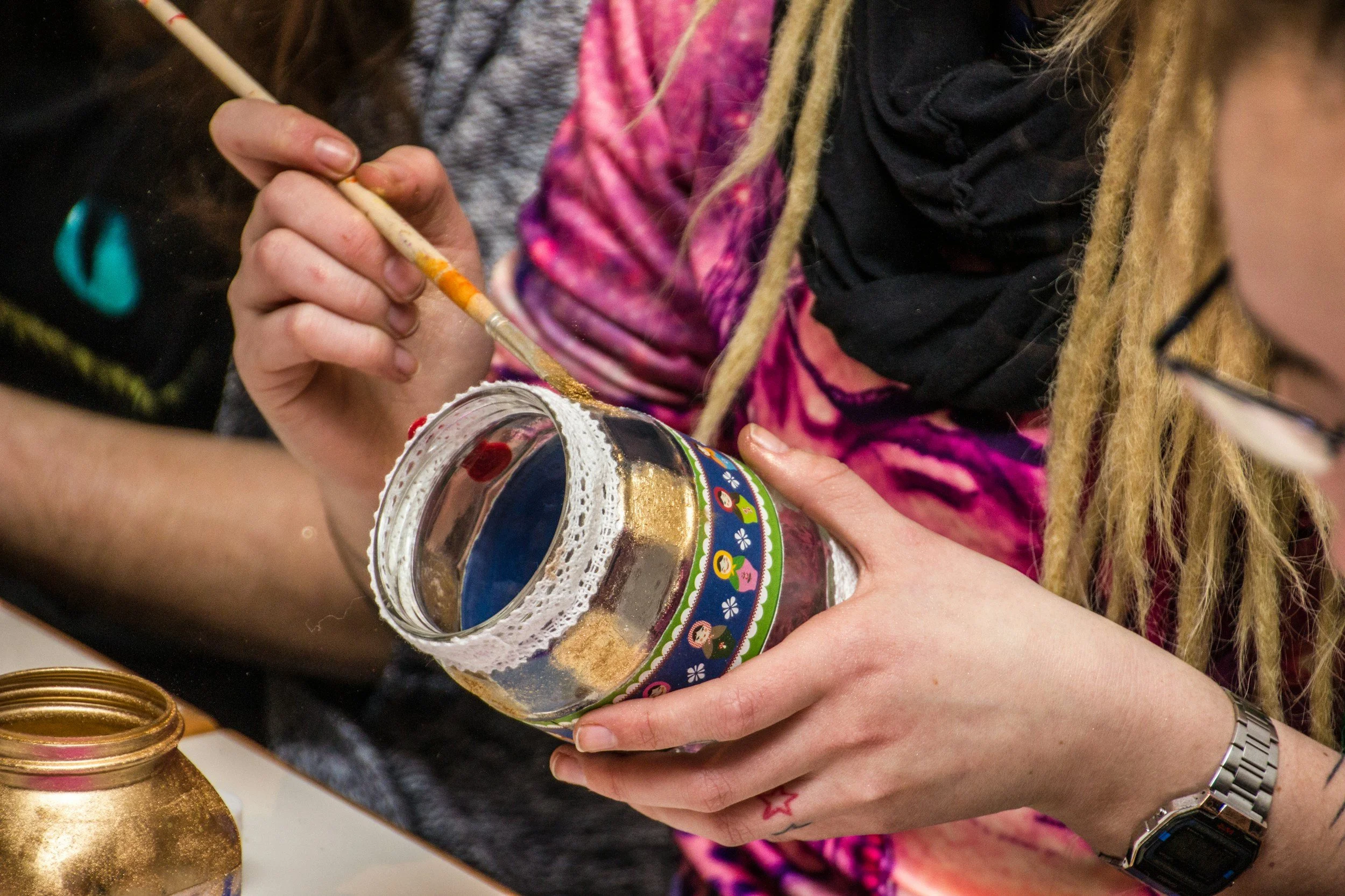 Person painting a decorative jar with gold paint using a small brush, with another gold-painted jar nearby.