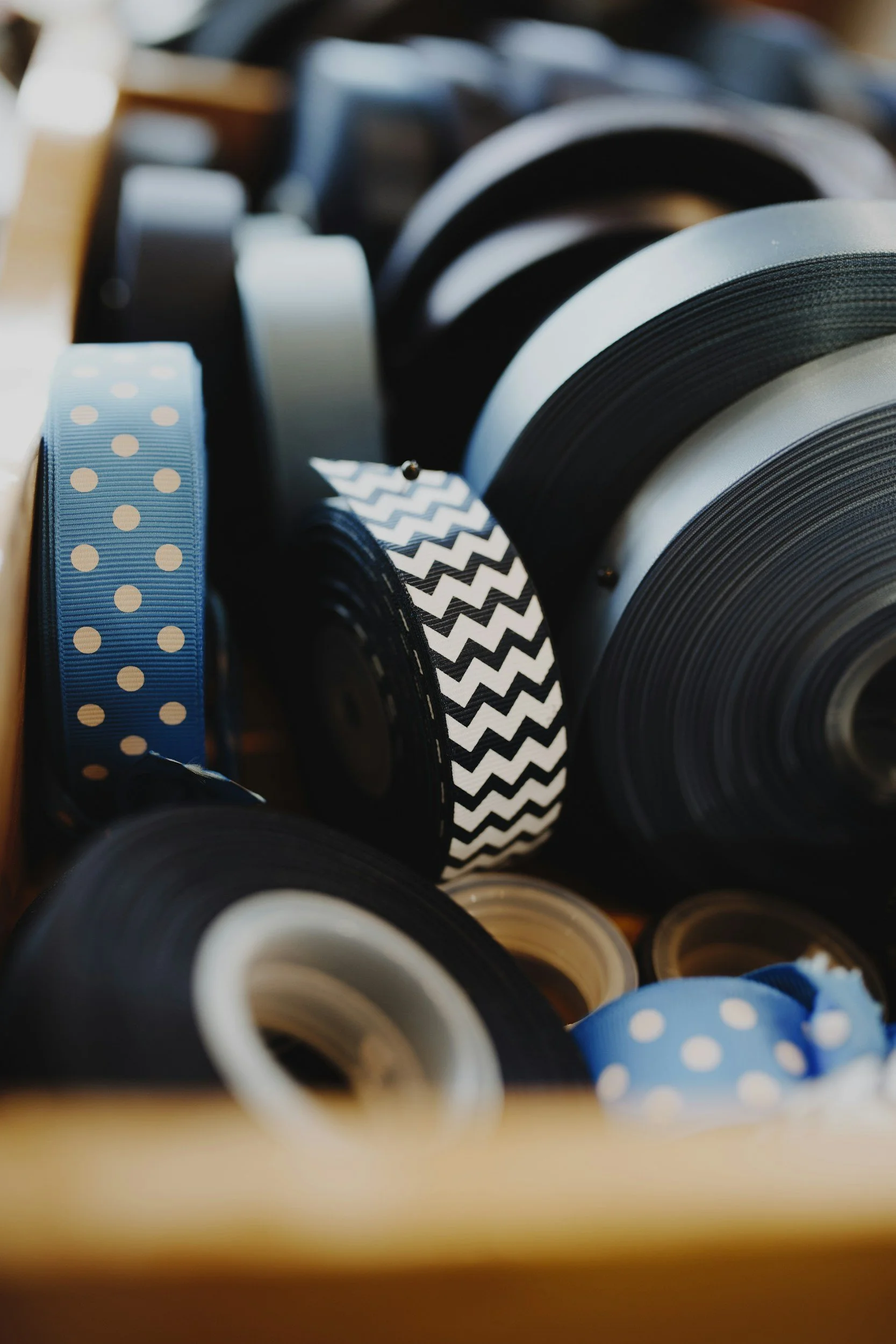 Spools of ribbon in various colors and patterns, including polka dots and chevrons, in a storage container.