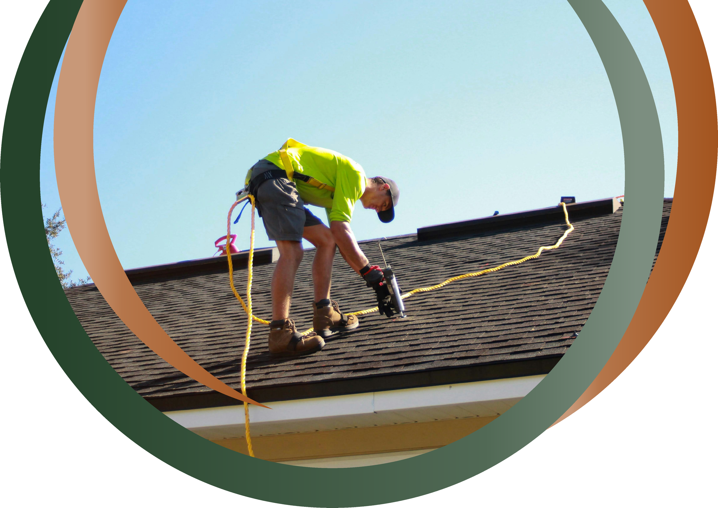 A man in a lime green shirt, gray shorts, and work boots is on a roof, using a power tool, secured by safety harness and ropes, with a clear blue sky background.
