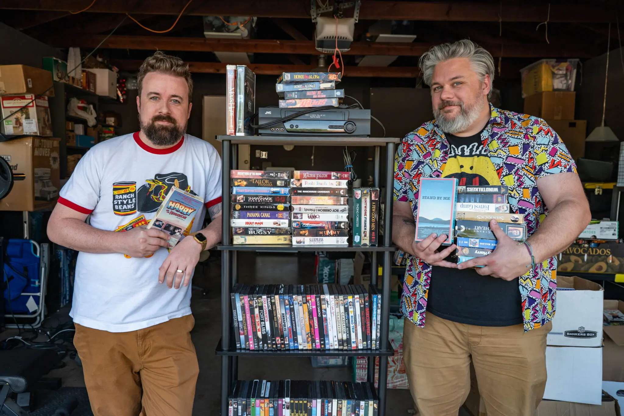 Jefferson Miller and Chris Emery stand next to a shelf of VHS and DVDs.
