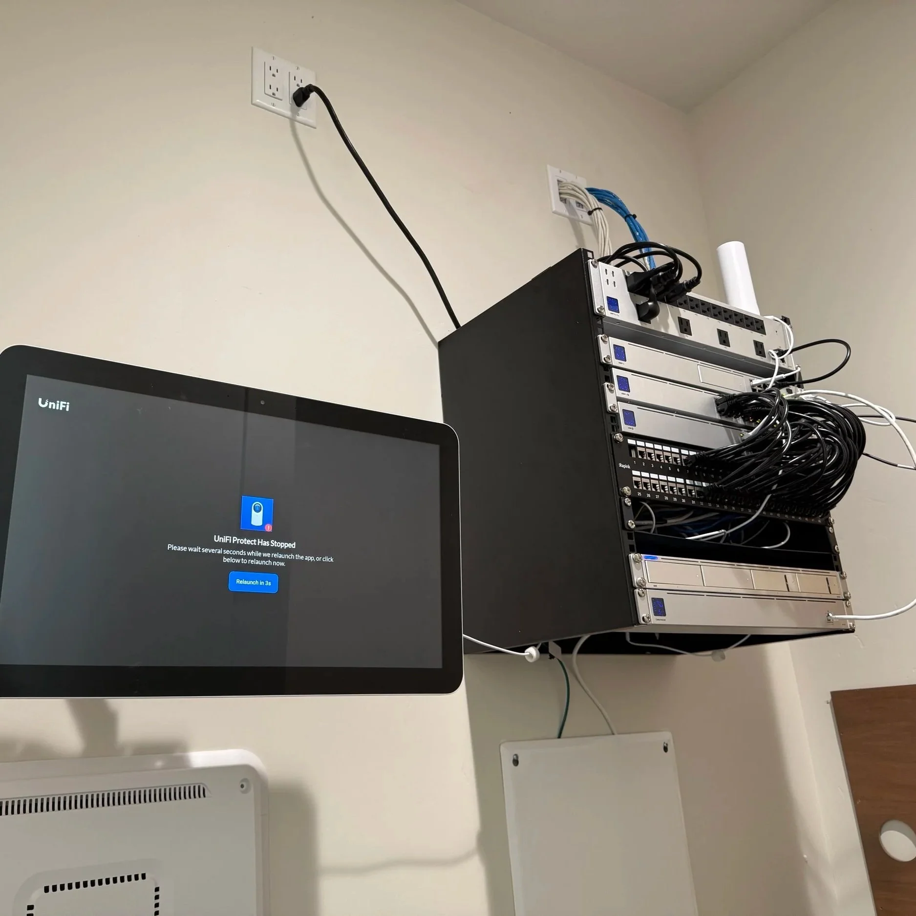 Computer monitor displaying a message that says 'UniFi Protect has stopped,' in a room with a server rack and various network cables connected to the rack.