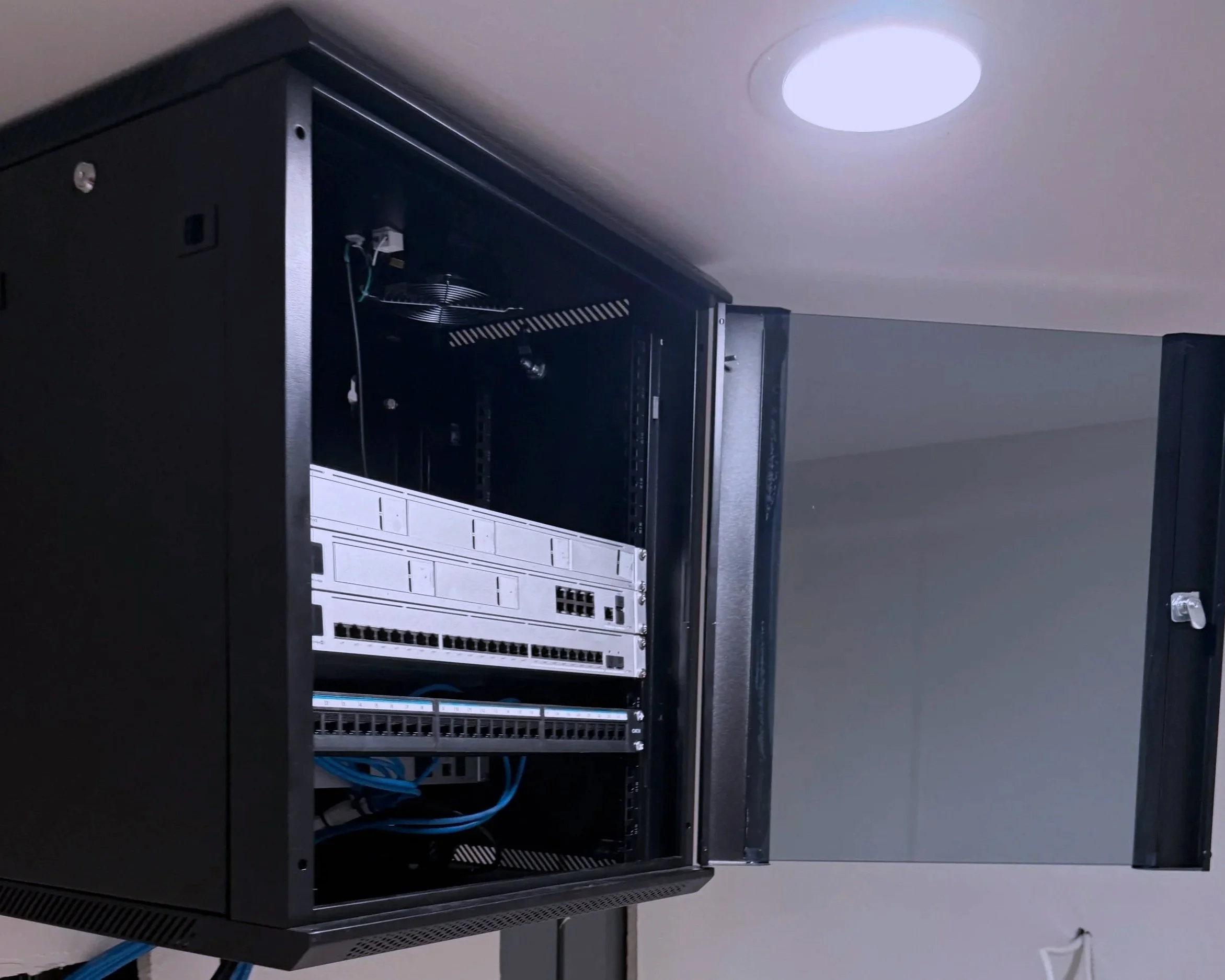 Open server rack with various network and server components inside, mounted on a wall in a data center.