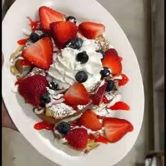 Dessert platter with whipped cream, strawberries, blueberries, raspberries, and chocolate shavings.