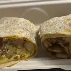 A burrito cut in half showing meat, vegetables, and other fillings inside a tortilla.