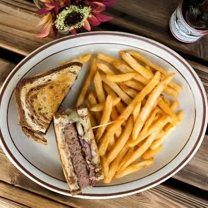 Club sandwich with French fries on a white oval plate, a bottle of soda in the background, and a small bouquet of flowers nearby.