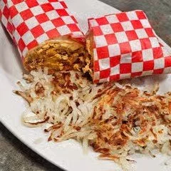 Two grilled cheese sandwiches wrapped in red and white checkered paper with shredded cheese and fried onions on a plate.