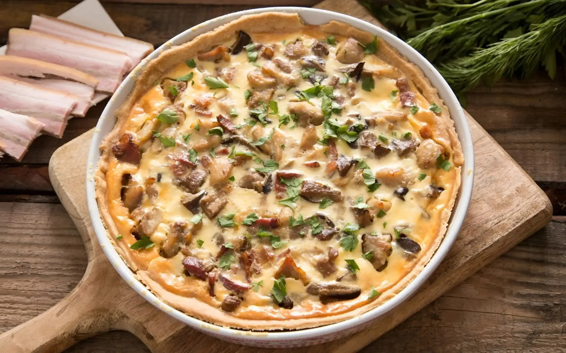Mushroom and bacon quiche topped with chopped parsley in a white pie dish