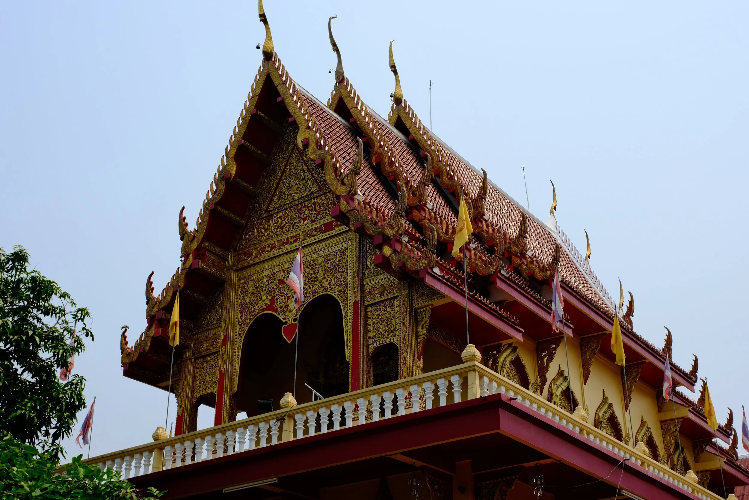 Detailed view of a traditional Thai temple with ornate golden decorations and a red roof, featuring multi-tiered gables and decorative finials.