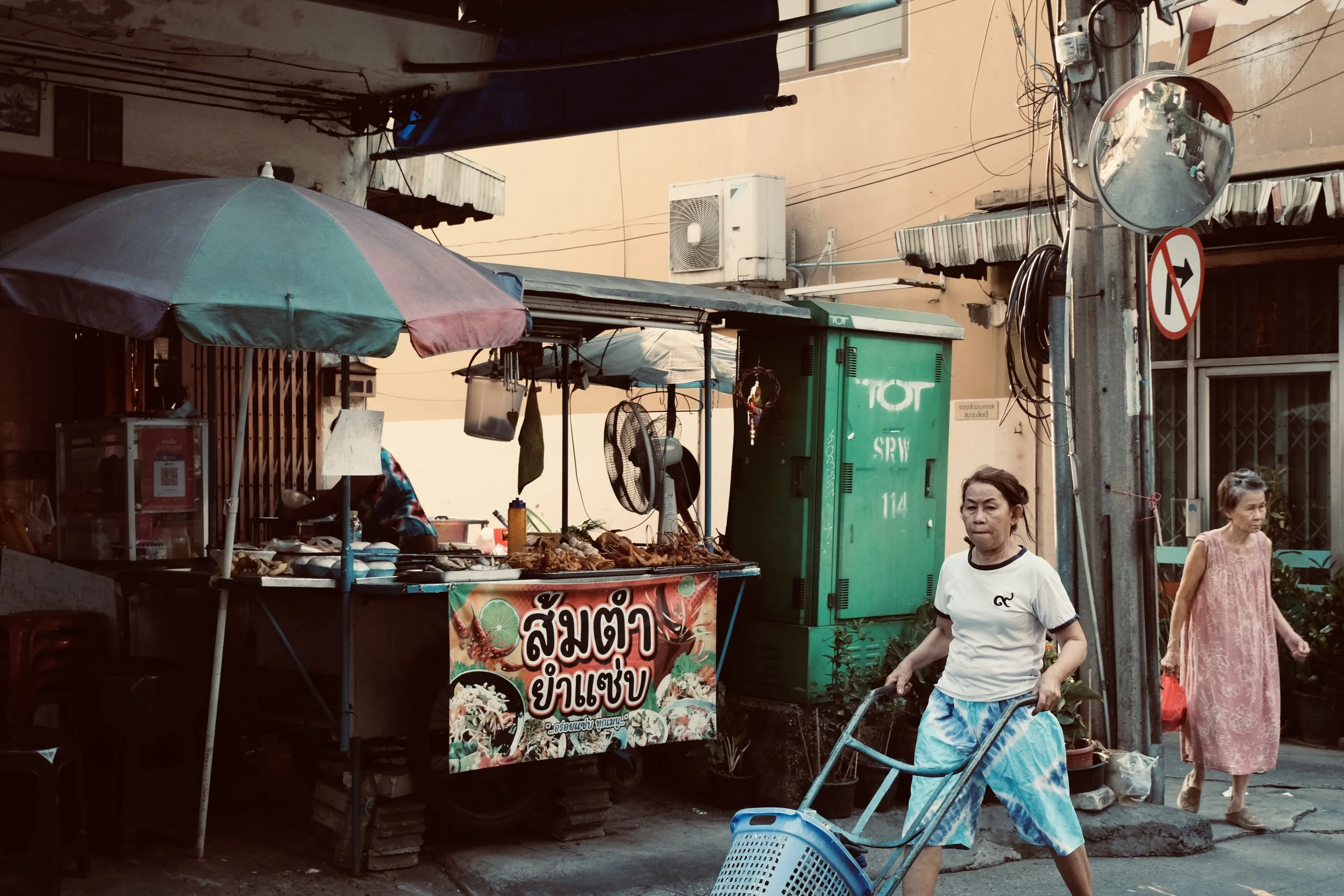 Street market scene with food stall, two women walking, and a street sign.