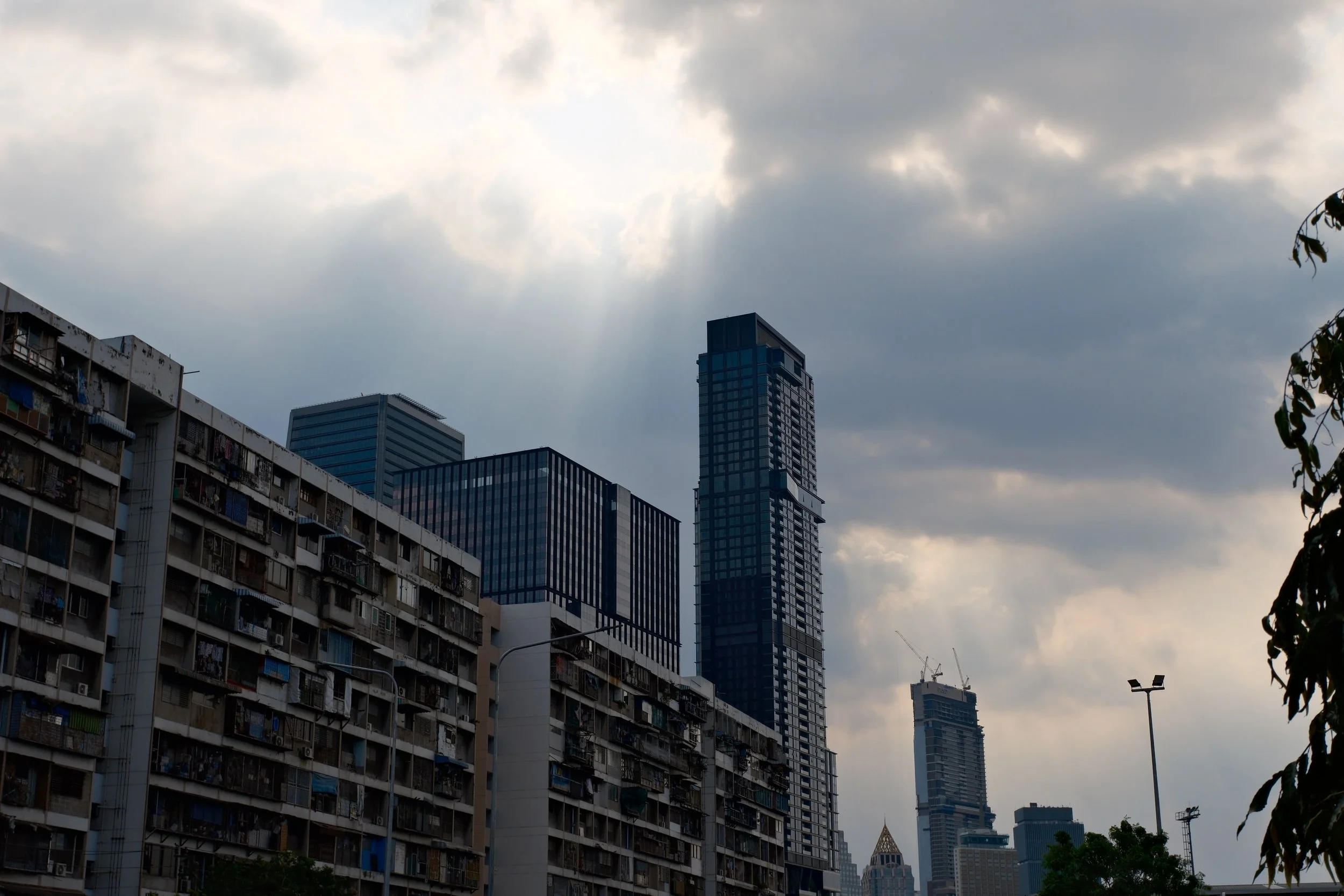 Cityscape with high-rise buildings under cloudy sky, including a tall modern skyscraper with glass windows and residential buildings with laundry hanging outside.