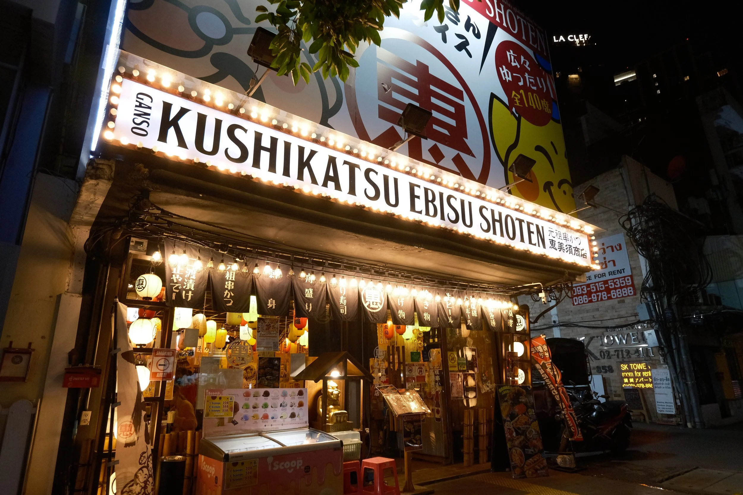 Exterior of Kushikatsu Ebisu Shoten restaurant at night, with illuminated sign, hanging lanterns, and menu boards outside.