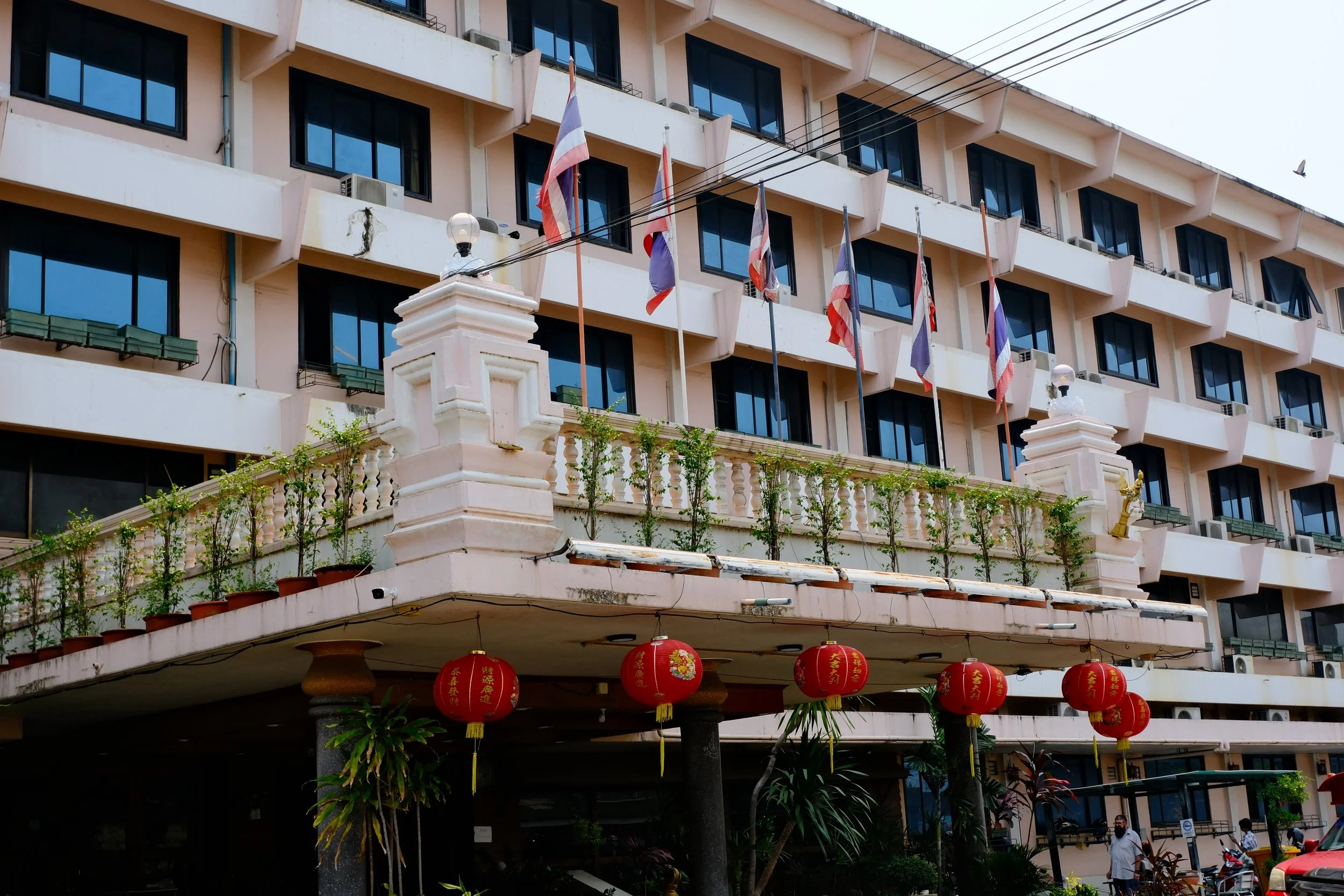 Exterior of a building with multiple balconies, flags, hanging lanterns, and plants.