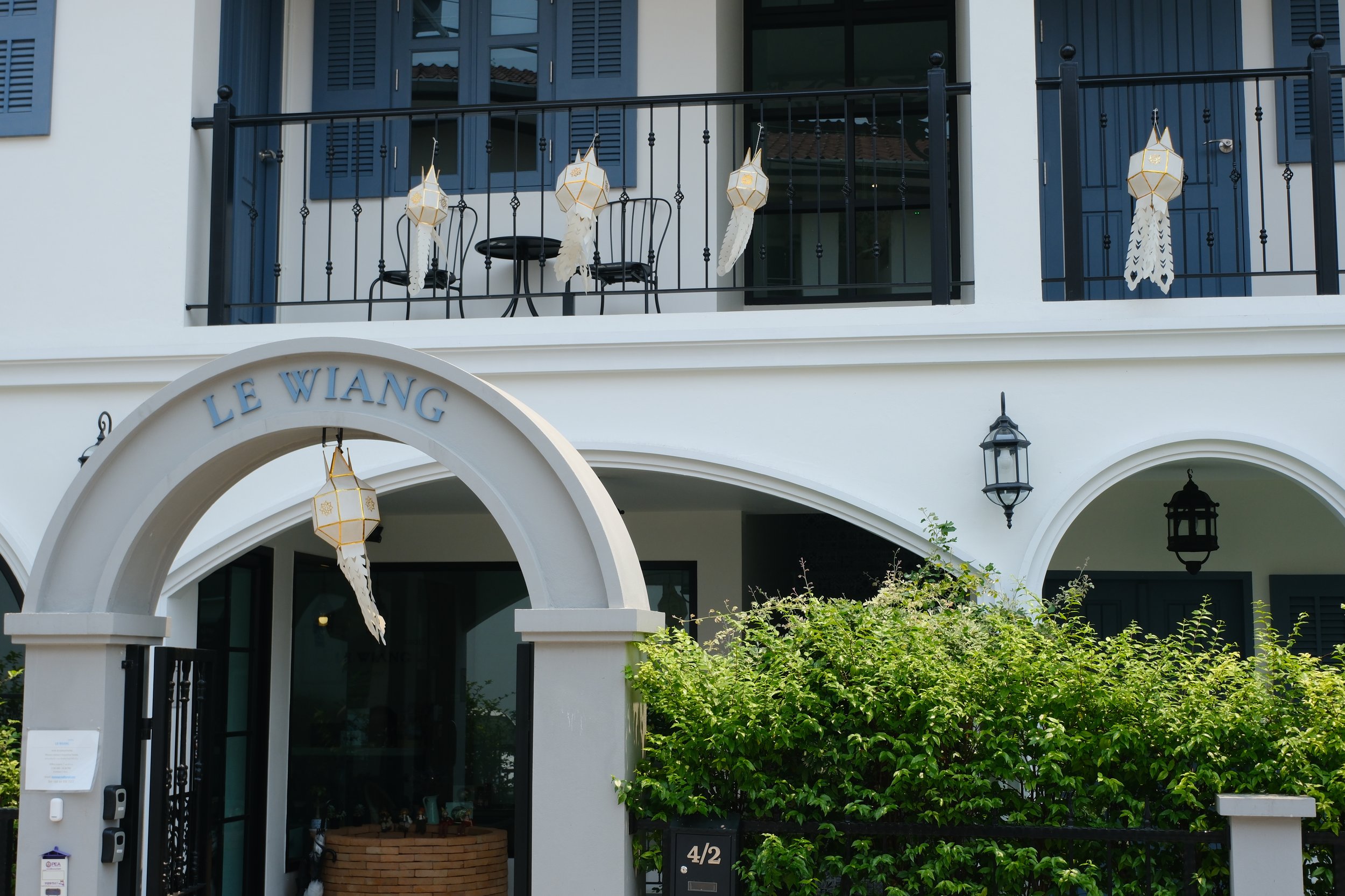 A white building with a black balcony, displaying hanging lantern decorations and outdoor lantern lights, and a sign reading 'Le Wian' above the entrance.