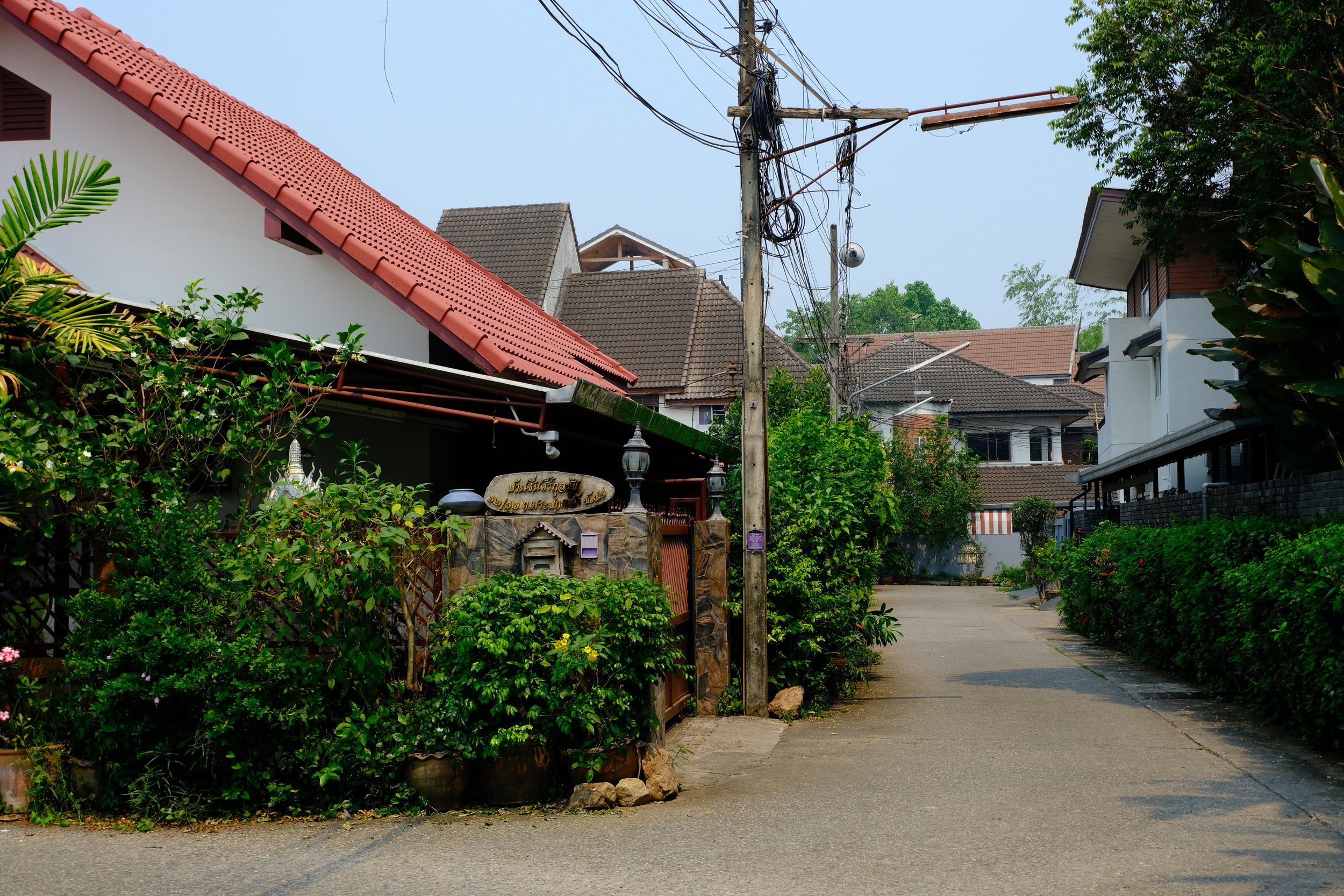 A quiet residential street with houses, greenery, and electrical wires.